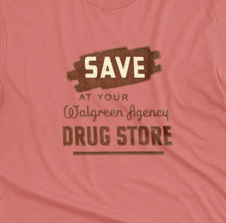 A coral pink t-shirt with a retro graphic print that reads 'SAVE AT YOUR Walgreen Agency DRUG STORE' from the 1960s.