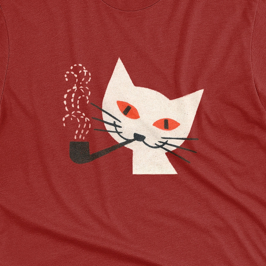 A red t-shirt with a graphic of a white cat smoking a pipe, featuring orange eyes and black whiskers. The image is from a 1950s matchbox cover.