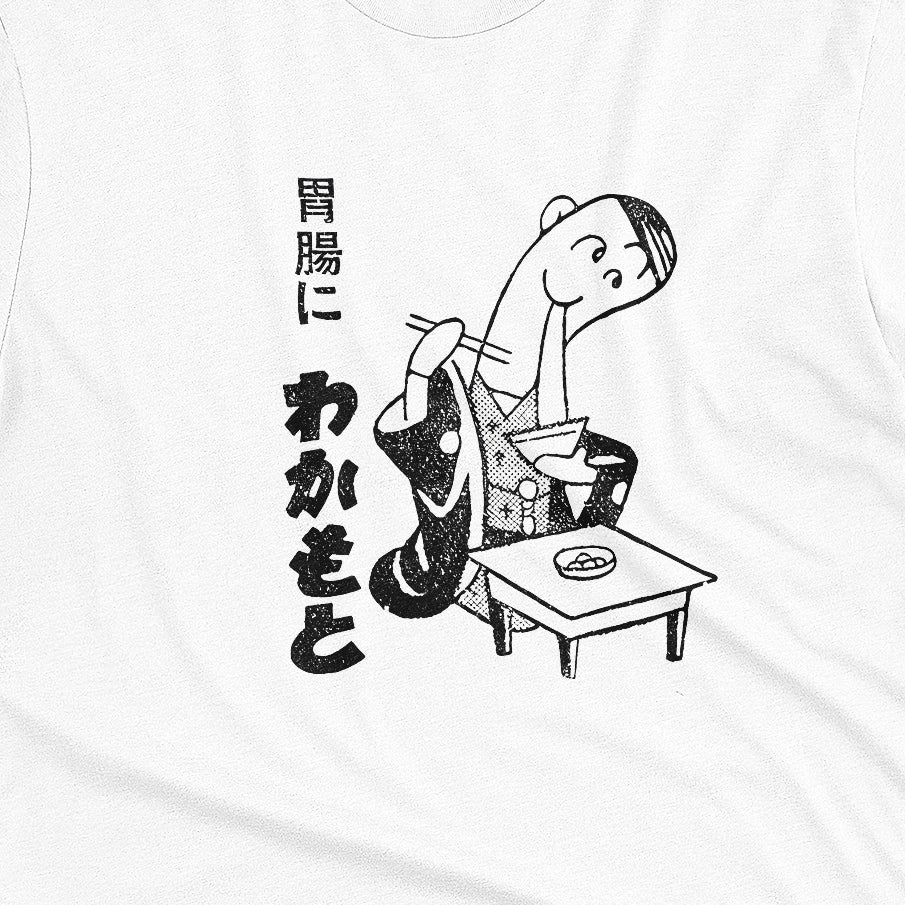 A white t-shirt with an advertisement for Wakamoto digestive tablets from a 1933 Japanese newspaper featuring a cartoon character in a kimono eating ramen next to Japanese text.
