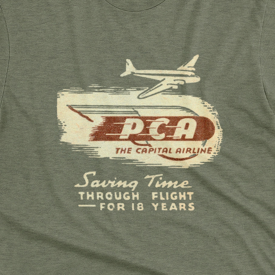 A green t-shirt featuring a vintage graphic advertisement for 'PCA THE CAPITAL AIRLINE'.