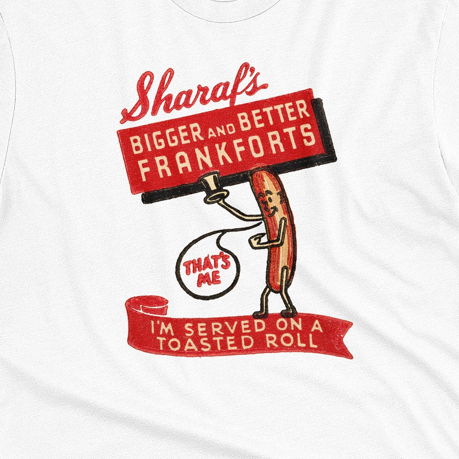 A white t-shirt with a vintage graphic print of a hot dog character holding a sign that reads 'Sharaf's Bigger and Better Frankforts'.