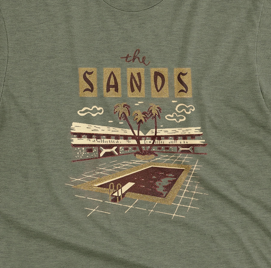 A green t-shirt with a retro advertisement for 'the SANDS' hotel featuring a poolside scene.