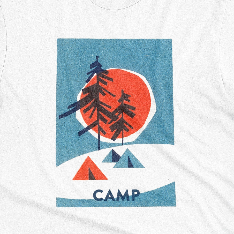 A white t-shirt featuring a 1960s retro-style graphic print of pine trees in front of a large orange-red sun within a blue square, with small orange and blue tents below and the word 'CAMP'.