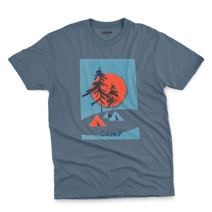 A blue t-shirt featuring a 1960s retro-style graphic print of pine trees in front of a large orange-red sun within a blue square, with small orange and blue tents below and the word 'CAMP'.