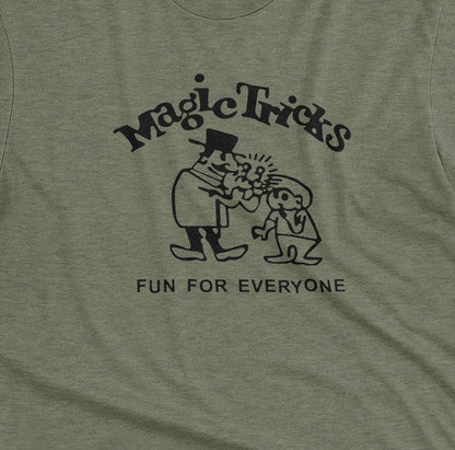 A green t-shirt with a black graphic print on the front that reads 'Magic Tricks' above a cartoon of a magician and a spectator, with 'FUN FOR EVERYONE' printed below.