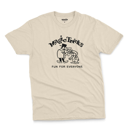 A beige t-shirt with a black graphic print on the front that reads 'Magic Tricks' above a cartoon of a magician and a spectator, with 'FUN FOR EVERYONE' printed below.