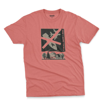 A coral pink t-shirt with a retro graphic print of an anti-war message featuring a cross, a plane, a house, and the text 'DON'T BOMB THINGS'.
