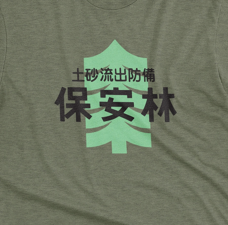 A green t-shirt with a Japanese graphic print featuring a light green pine tree and black text saying 'Landslide Protected Forest' in Japanese.