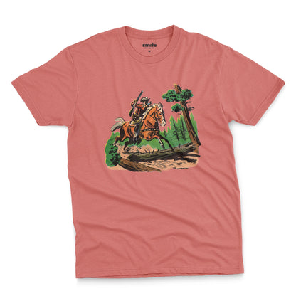 A coral pink t-shirt featuring a 1960s vintage graphic print of a cowboy riding a horse through a forest.