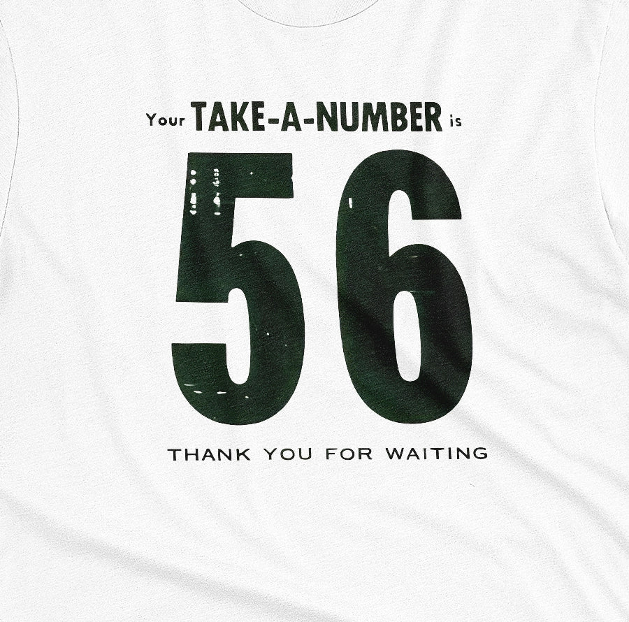 A white t-shirt with a 1960s retro graphic reading 'Your TAKE-A-NUMBER is 56 THANK YOU FOR WAITING' in distressed typography.