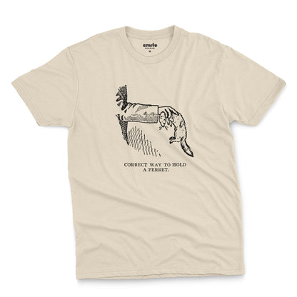 A beige t-shirt with a vintage engraved illustration of an arm holding a ferret and text saying: Correct way to hold a ferret.