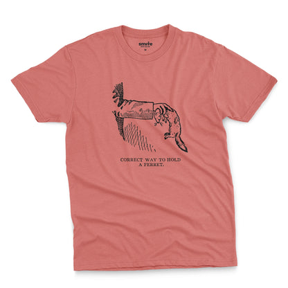 A coral pink t-shirt with a vintage engraved illustration of an arm holding a ferret and text saying: Correct way to hold a ferret.