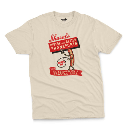 A beige t-shirt with a vintage graphic print of a hot dog character holding a sign that reads 'Sharaf's Bigger and Better Frankforts'.