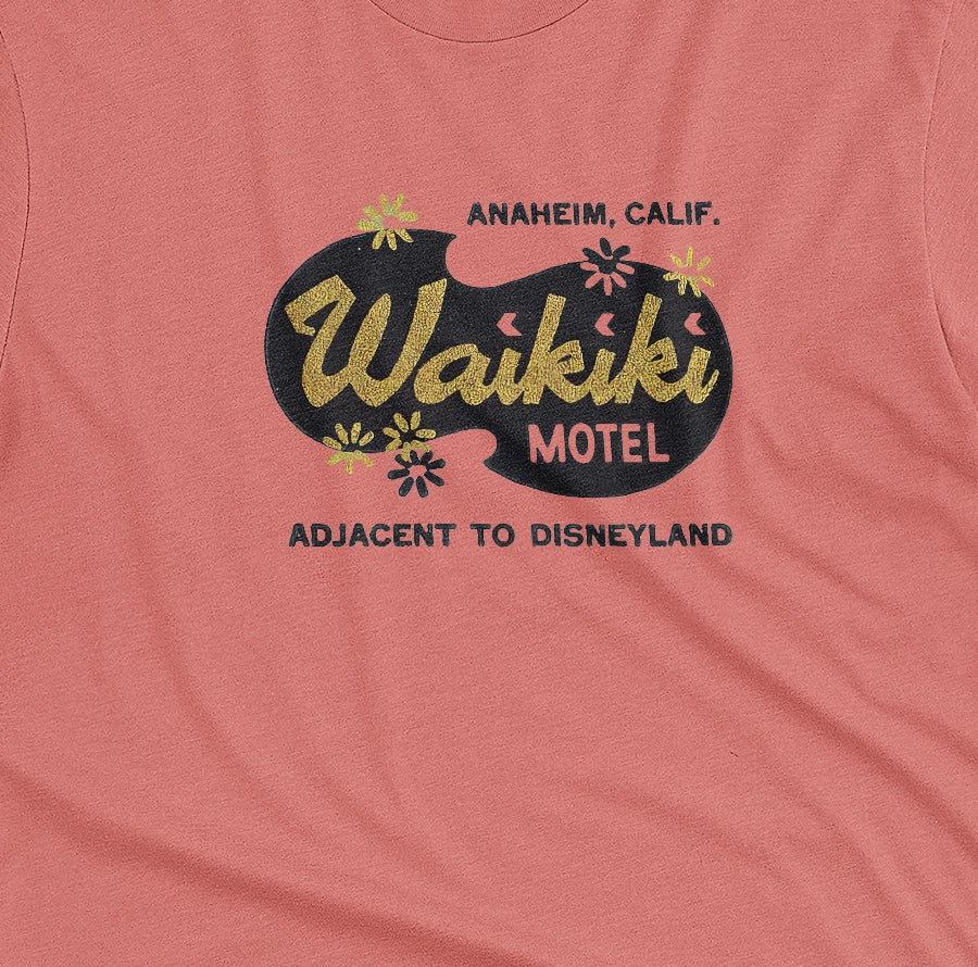 A coral pink t-shirt with a retro advertisement for the 'Waikiki Motel' in Anaheim, California.