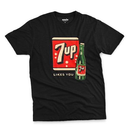A black t-shirt featuring a retro advertisement for 7up with the text '7up LIKES YOU'.