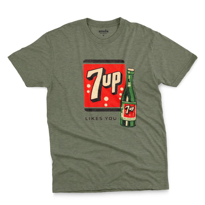 A green  t-shirt featuring a retro advertisement for 7up with the text '7up LIKES YOU'.