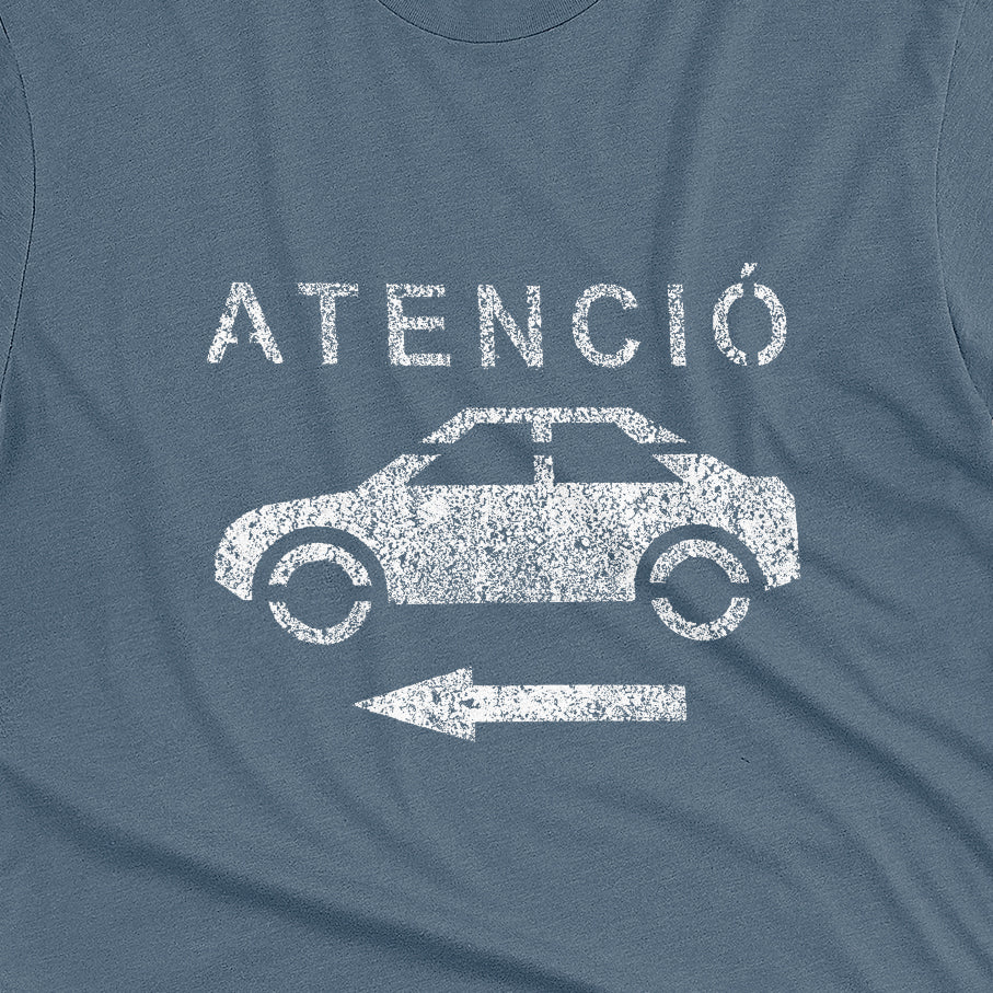 A blue t-shirt with a retro white stencil graphic of a car and the Spanish word 'ATENCIÓ'.
