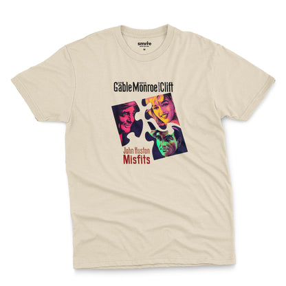 A beige t-shirt featuring a colorful graphic advertisement for the movie The Misfits starring Clark Gable, Marilyn Monroe, and Montgomery Clift.